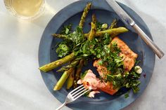 a blue plate topped with salmon and asparagus next to a glass of wine