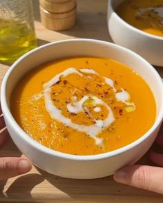 two hands holding a bowl of carrot soup