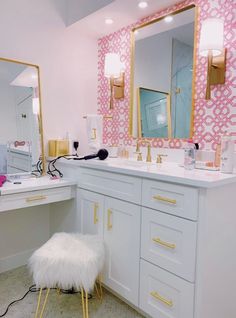 a pink and white bathroom with gold accents on the vanity, mirror, and stool