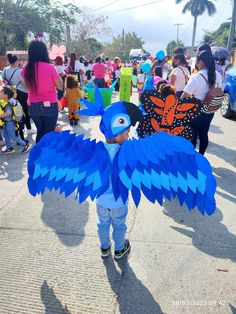 a little boy wearing a blue bird costume on the street with people in the background