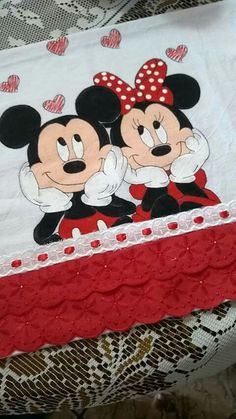 two mickey and minnie mouses on a white sheet with red lace trim around the edges