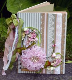 an open book with flowers and ribbons on the cover, sitting in front of some plants