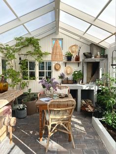 a room filled with lots of potted plants next to a table and chairs in front of a window