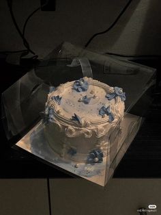 a white cake with blue flowers on it in a clear plastic box sitting on top of a table