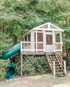 a tree house with a slide in front of it and lots of trees surrounding it