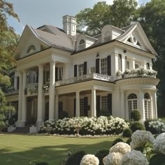 a large white house surrounded by trees and flowers