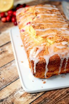 a loaf of lemon pound cake with icing on a white plate next to some cranberries