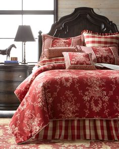 a bed with red and white comforters in a bedroom next to a dresser, lamp and window