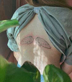 the back of a woman's head with two wings on her upper body and behind her is a green plant