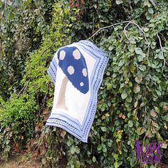 a blue and white mushroom quilt hanging from a tree in front of some green bushes