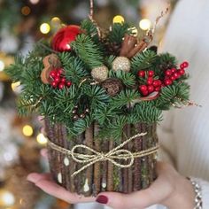 a woman is holding a christmas decoration in her hand, with pine cones and berries on it