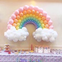 a rainbow shaped balloon is above a table with many desserts and drinks on it