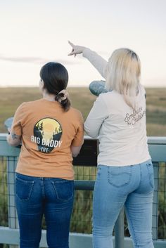 two women standing on a bridge pointing at the sky