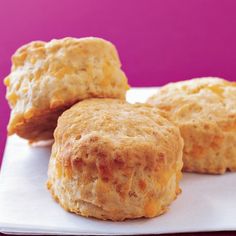 three biscuits sitting on top of a white plate next to a purple background and pink backdrop