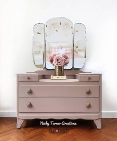 a pink dresser with three mirrors and a flower on it in front of a white wall