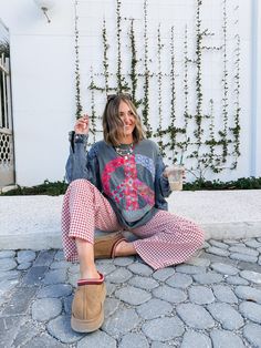 a woman sitting on the ground with her legs crossed and holding a drink in one hand