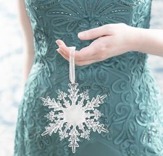 a snowflake ornament being held by a woman in a green dress