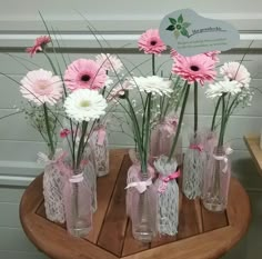 pink and white flowers are in glass vases on a wooden table next to a sign