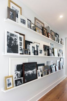 a wall filled with lots of pictures and framed photos next to a hard wood floor