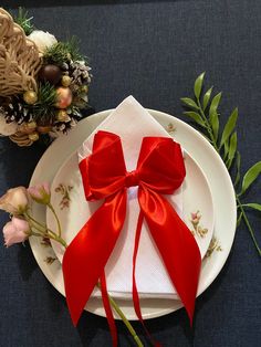 a plate with a red bow on it next to some flowers and greenery in the background