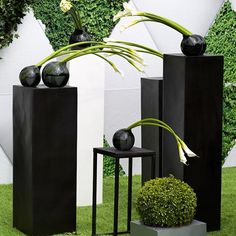 three black vases with flowers in them sitting on the grass next to each other