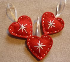 three red hearts with white stars on them hanging from silver ribbon and two other heart shaped ornaments