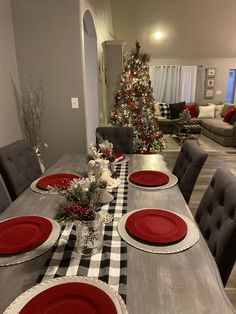 a dining room table set for christmas with red plates and placemats on it