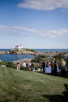 a group of people standing on top of a lush green field next to the ocean