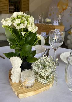 a table topped with white flowers and vases filled with greenery on top of a wooden tray