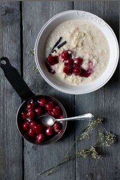 two bowls of oatmeal with cherries and spoons on a wooden table