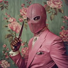 a man in a pink suit and mask holding a knife up to his face with both hands