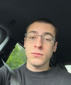 a man with glasses sitting in the back seat of a car looking at the camera