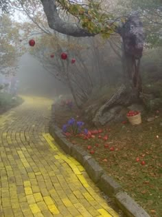 a yellow brick path in the fog with red apples hanging from it's branches