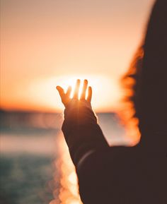 a person holding their hand up to the sun