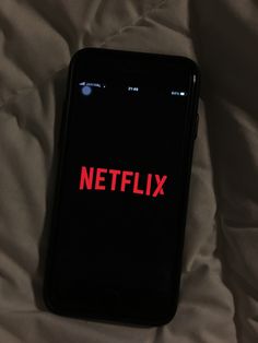 a black cell phone with the netflix logo on it sitting on a white bed sheet