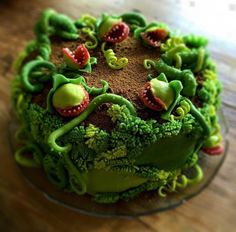 a cake decorated with green and red decorations on a wooden counter top, including broccoli