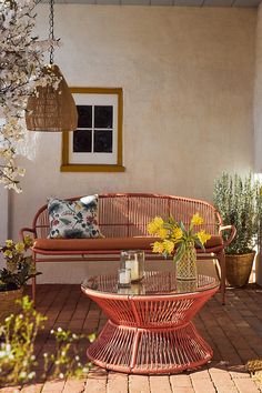 a red wicker couch sitting on top of a brick floor next to a potted plant