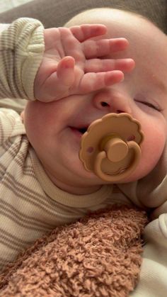 a smiling baby with a pacifier in it's mouth and his hand on the nose