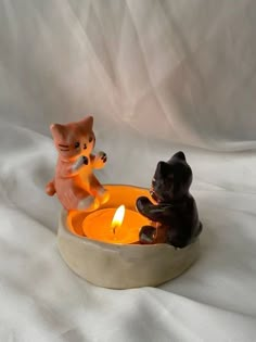 two cats sitting in a bowl with a lit candle