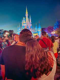 people standing in front of a castle at night with the lights on and buildings lit up