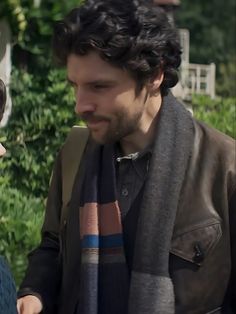 a man and woman standing next to each other in front of some bushes looking at something