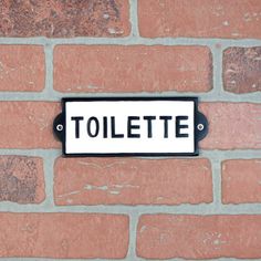 a black and white sign on a brick wall that says tolete in english