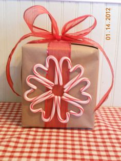 a gift wrapped in brown paper and tied with red ribbon on top of a checkered tablecloth