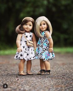 two dolls standing next to each other on a gravel road with trees in the background