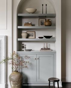 a shelf with vases, bowls and pictures on it in a living room area