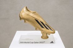 a gold soccer shoe on display in front of a gray background with the words world cup qatar written below it