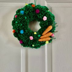 a green wreath with carrots and pom - poms hanging on the front door