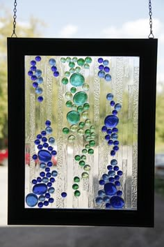 a stained glass window with blue and green beads hanging from it's side on a chain