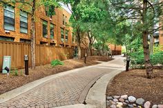 a brick walkway between two buildings with trees on both sides and rocks in the middle