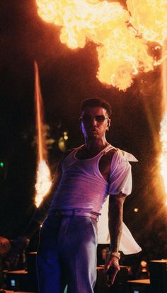 a man standing in front of a large fire with his hands on his hips while wearing sunglasses